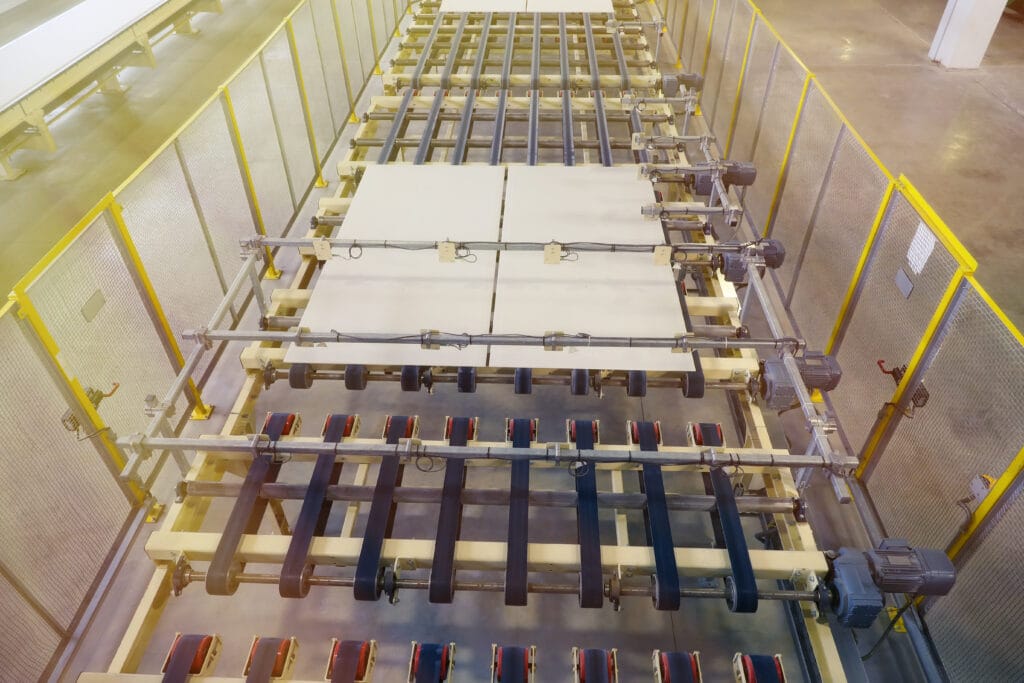 Overhead view of roller-and-belt conveyor moving flat panels inside Hi‑Vac Industrial plant, yellow safety fencing
