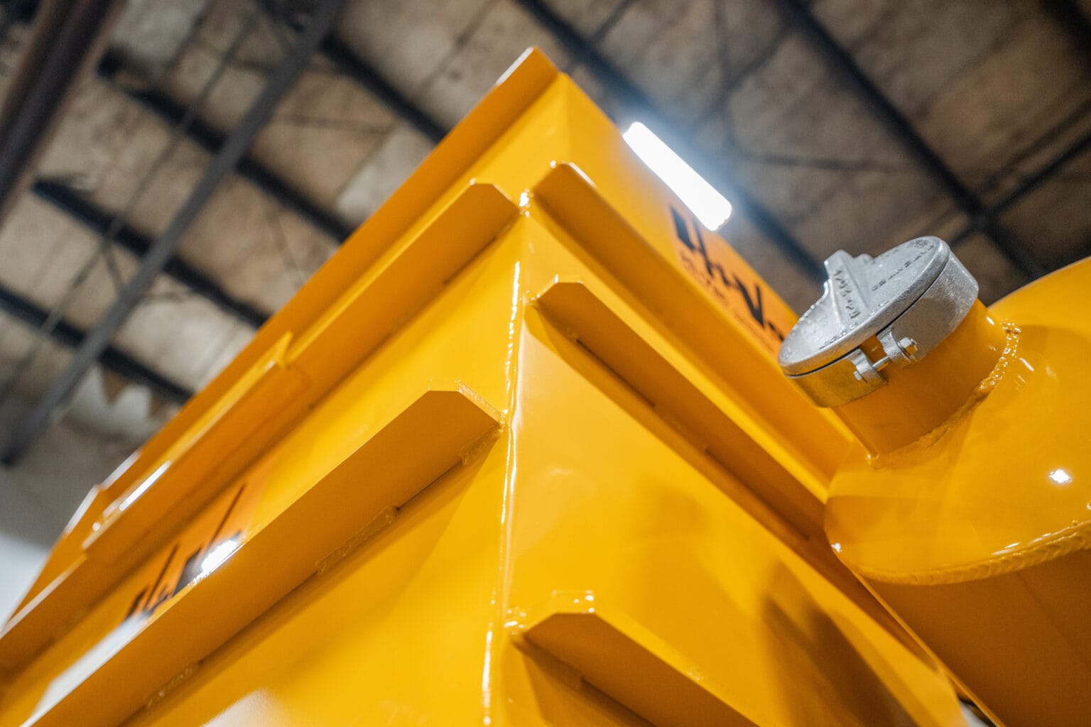 Bright yellow welded metal corner with reinforced ribs and a round filler cap on a Hi‑Vac industrial vacuum tank