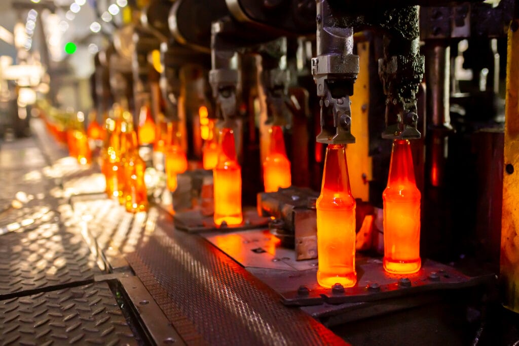 Glowing glass bottles on an automated production line under mechanical molds, part of industrial manufacturing.