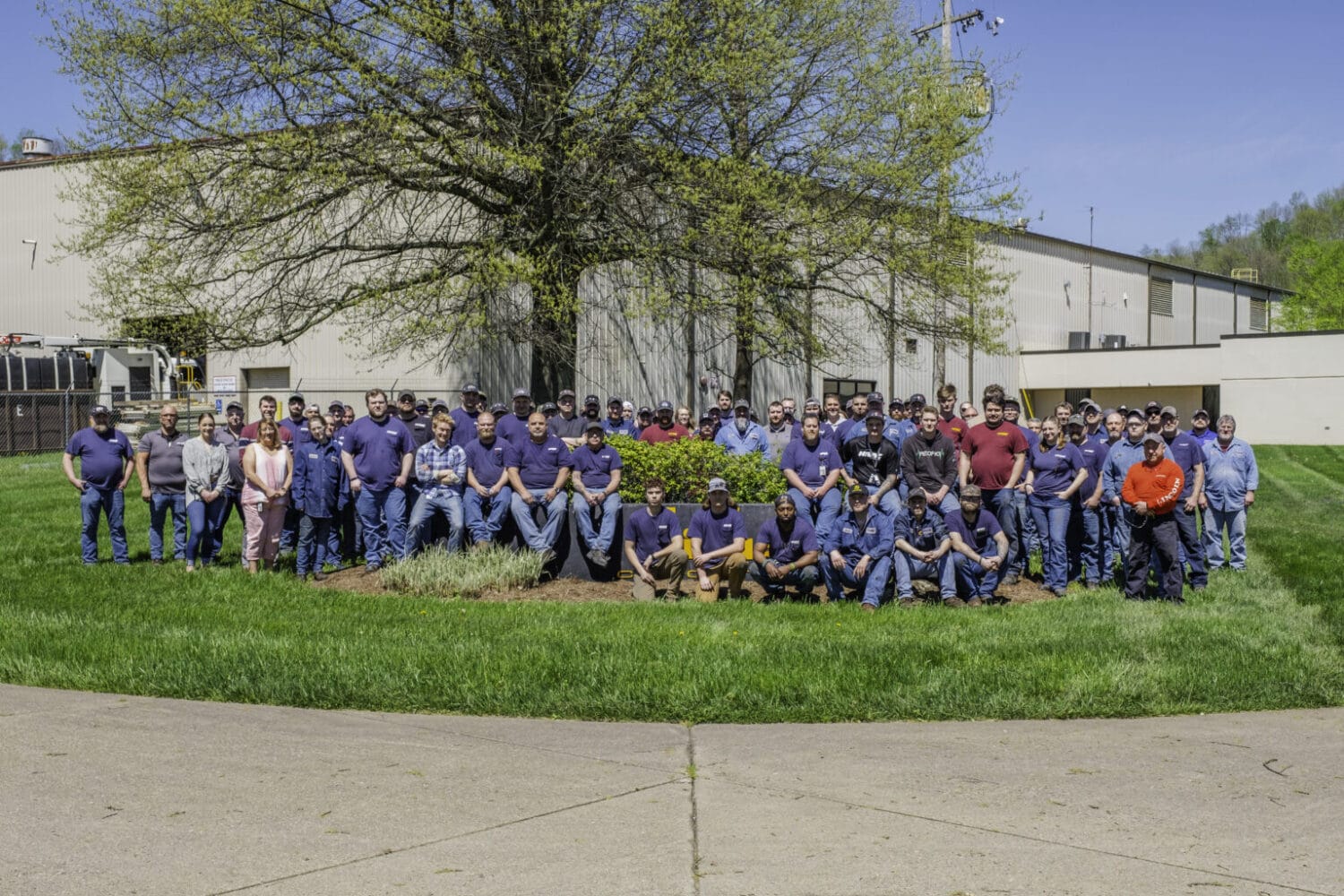 Large group of Hi-Vac Industrial employees posed outside manufacturing plant beneath a tree, vacuum truck fabrication team.