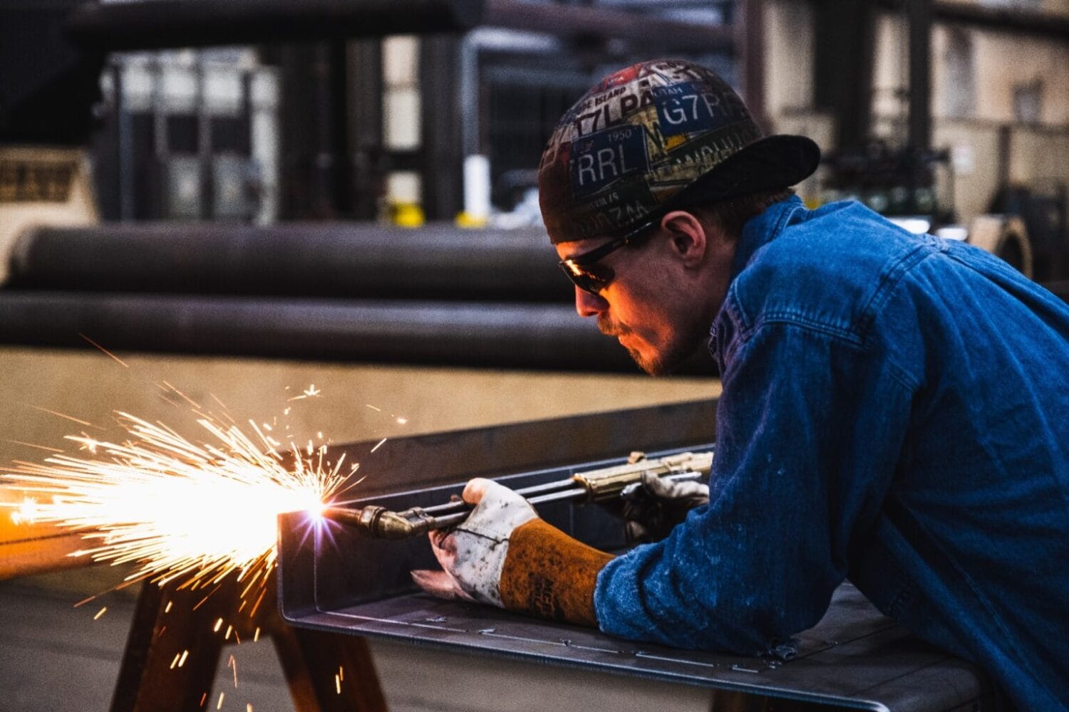 Welder cutting steel channel with torch, sparks flying during precision fabrication in an industrial shop