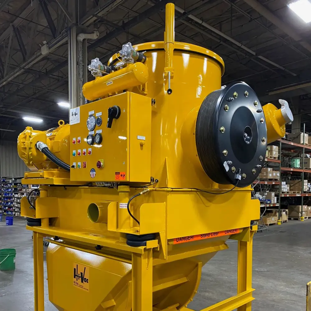 Bright yellow Hi-Vac industrial vacuum module with control panel, hose reel and cyclone hopper in a factory warehouse.