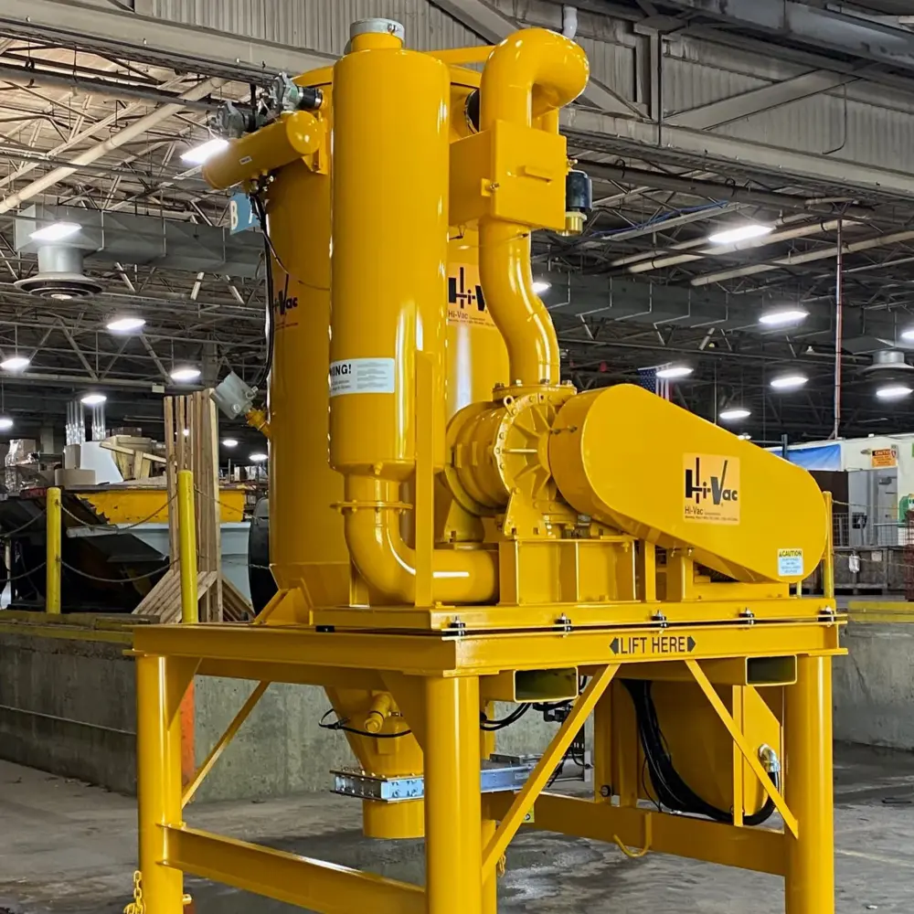 Bright yellow Hi-Vac industrial vacuum skid with blower, cyclonic piping and lift-frame in a factory assembly area.